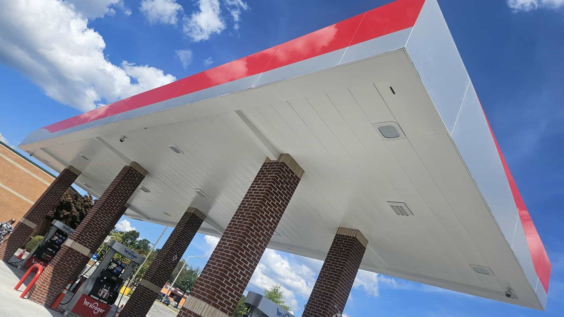Gas station canopy with red and white roof, supported by brick columns, against a blue sky.