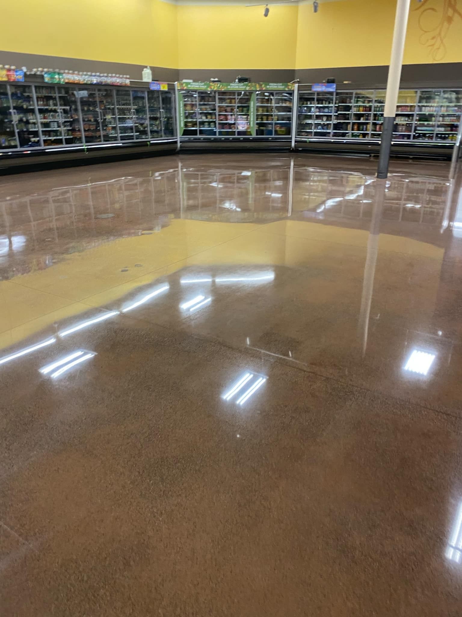 Polished concrete floor in a store, reflecting overhead lights and shelves of products in the background.
