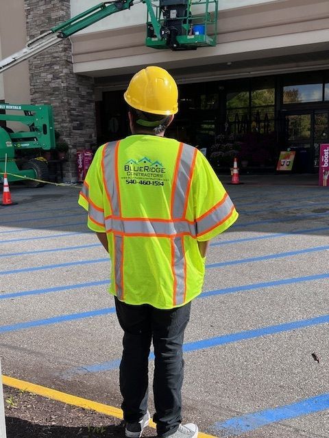 Person in reflective vest and hard hat observes work being done on building facade from a lift. Person in reflective vest and hard hat observes work being done on building facade from a lift.
