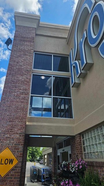 Exterior of a Kroger grocery store. Brick facade with large windows; blue sky reflects in glass. Kroger sign.