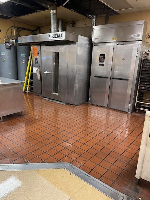 Commercial kitchen with oven, refrigerator, and red tile floor.