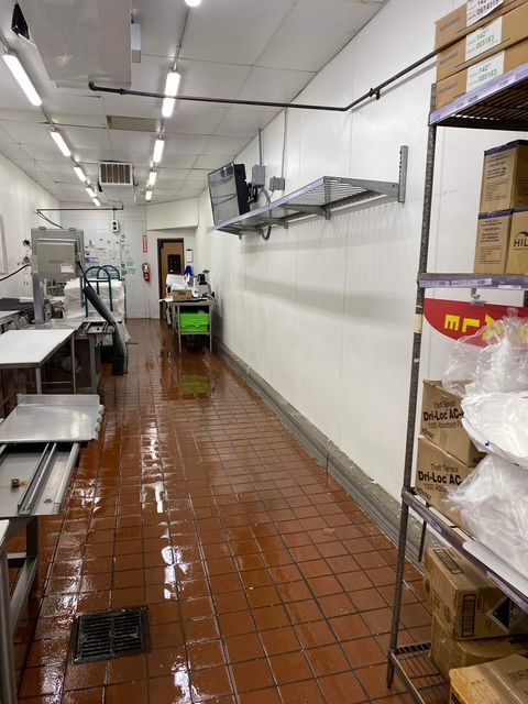 A commercial kitchen with stainless steel counters and red tile floor; a shelf with boxes on the right.