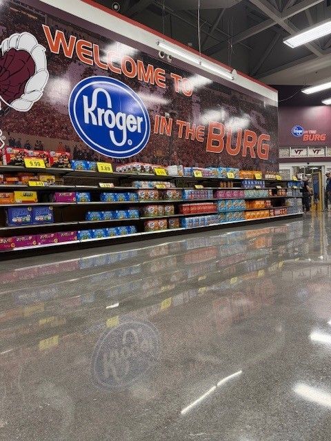 Kroger store interior with Welcome to Kroger in the Burg sign above shelves stocked with merchandise. Shiny floor.
