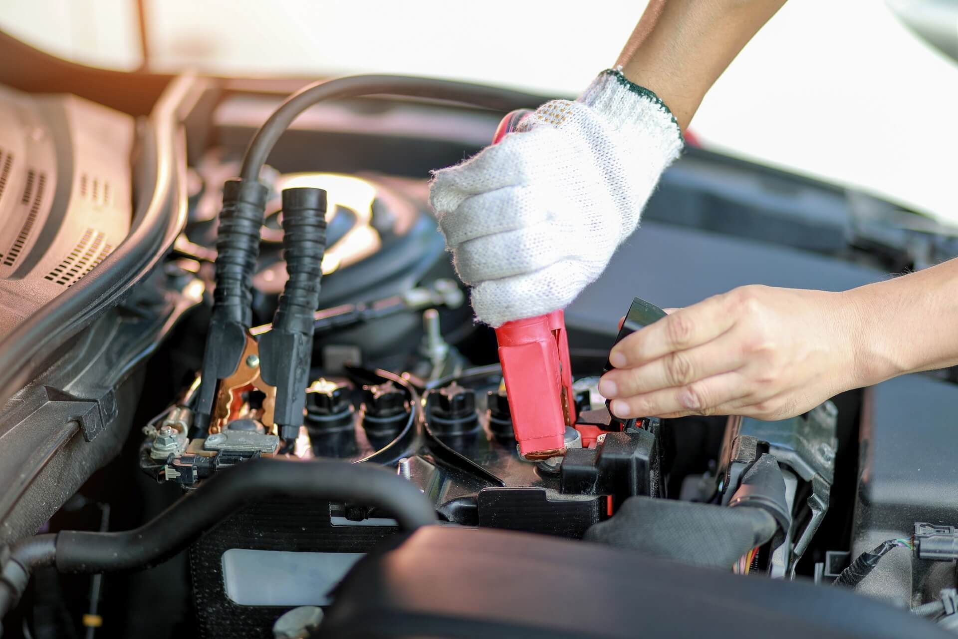 A completely dead car battery being boosted by a roadside assistance technician.