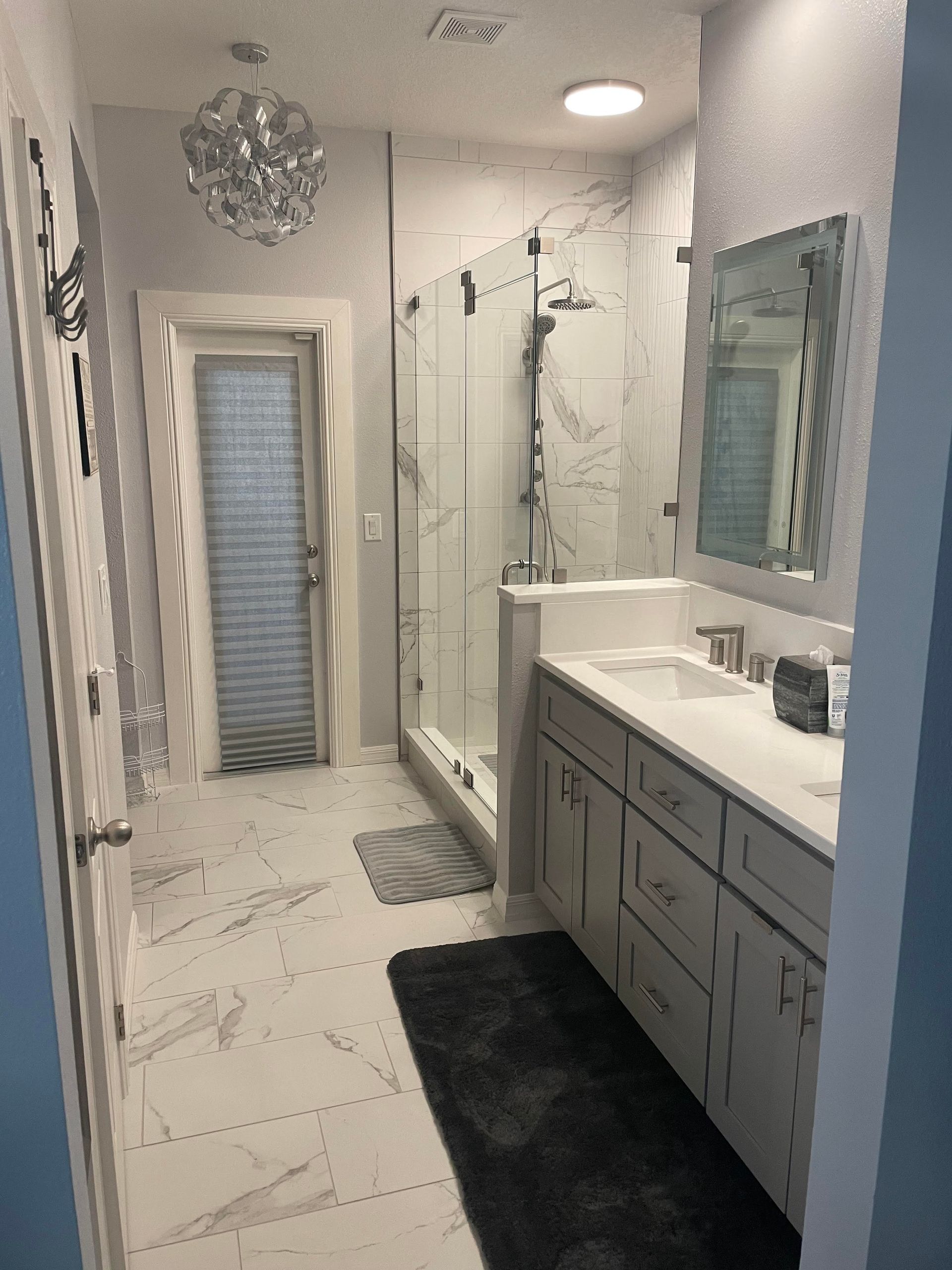 Bathroom remodel in Wright, Florida featuring brand new tile floors, an extraordinary and unique hanging light fixture, LED mirrors, quartz countertops