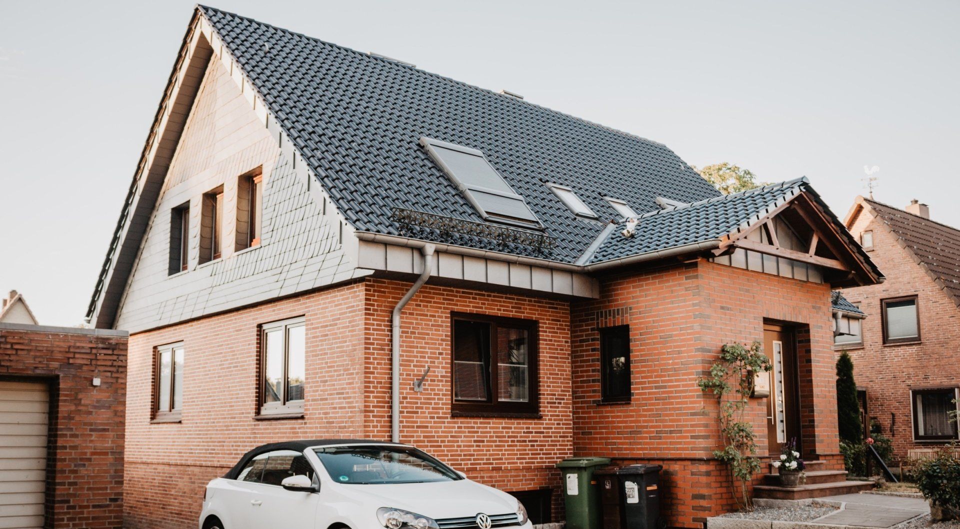 A white car is parked in front of a brick house.
