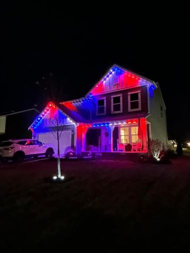 A two-story suburban house at night, decorated with patriotic red, white, and blue exterior lights.