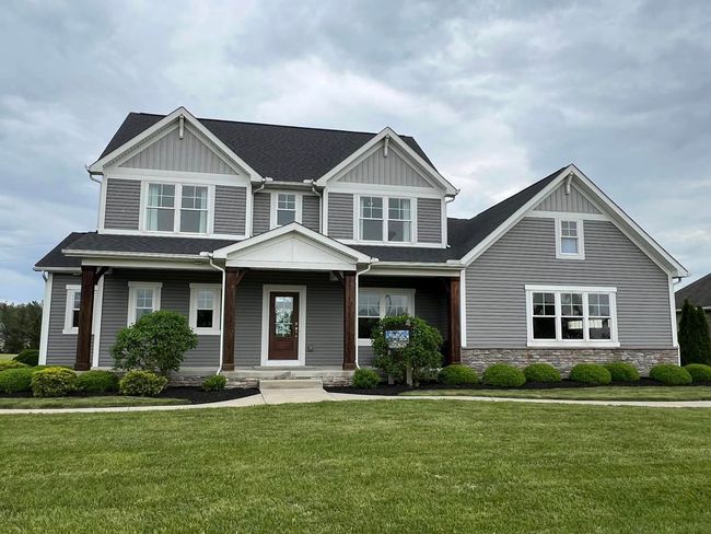 A two-story suburban house with grey horizontal siding, a stone base, a dark shingled roof, and a covered front porch.