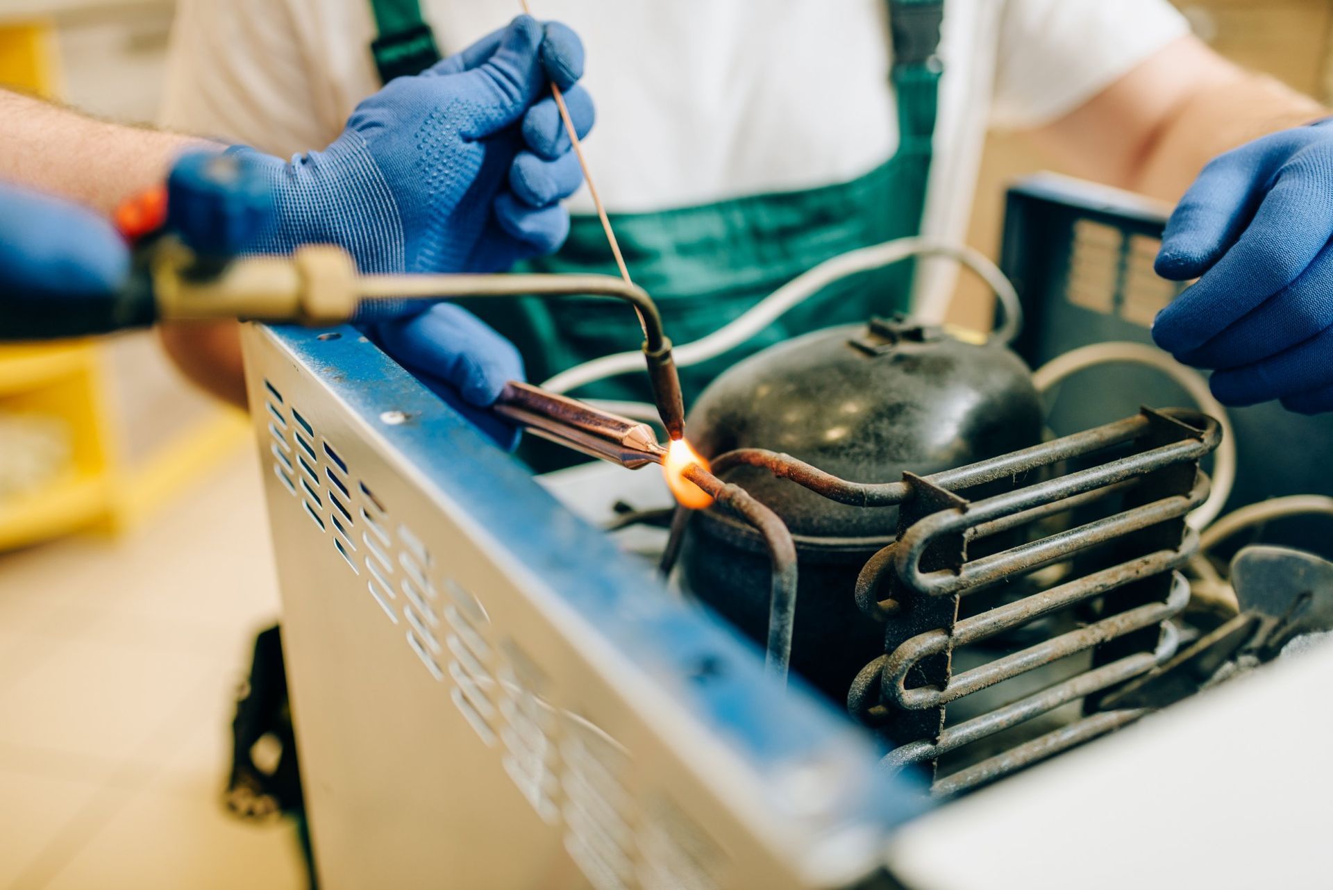 Hands in blue gloves soldering refrigerator components with a torch.