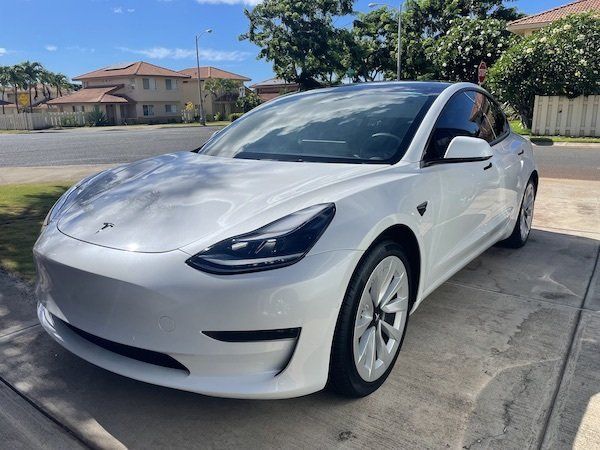 A white tesla model 3 is parked on the side of the road.