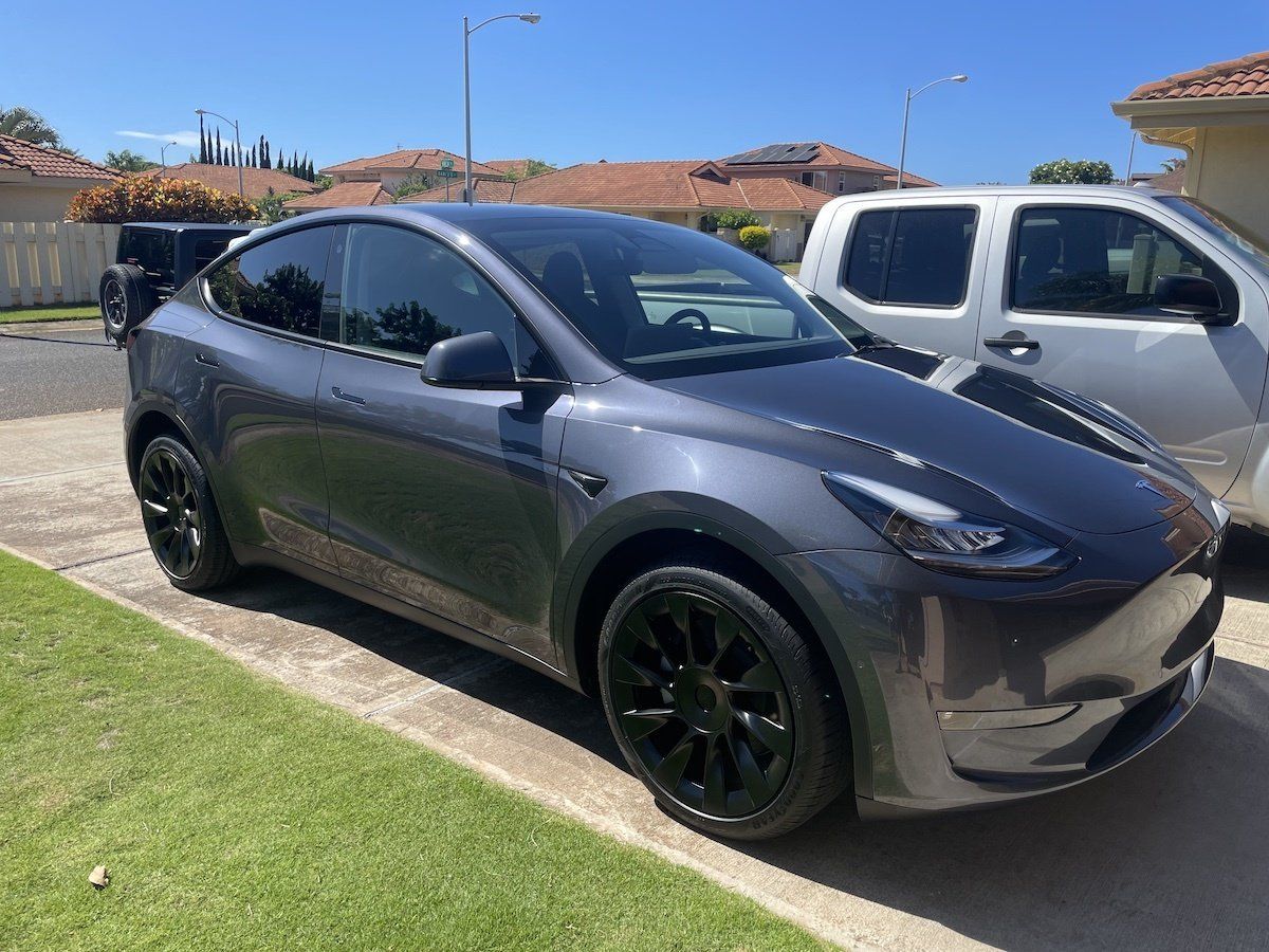 A tesla model y is parked in a driveway next to a truck.
