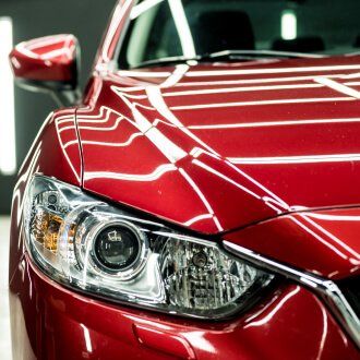 A close up of a red car 's headlight and hood