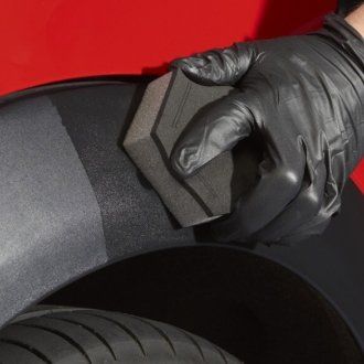 A person wearing black gloves is cleaning a car with a sponge.