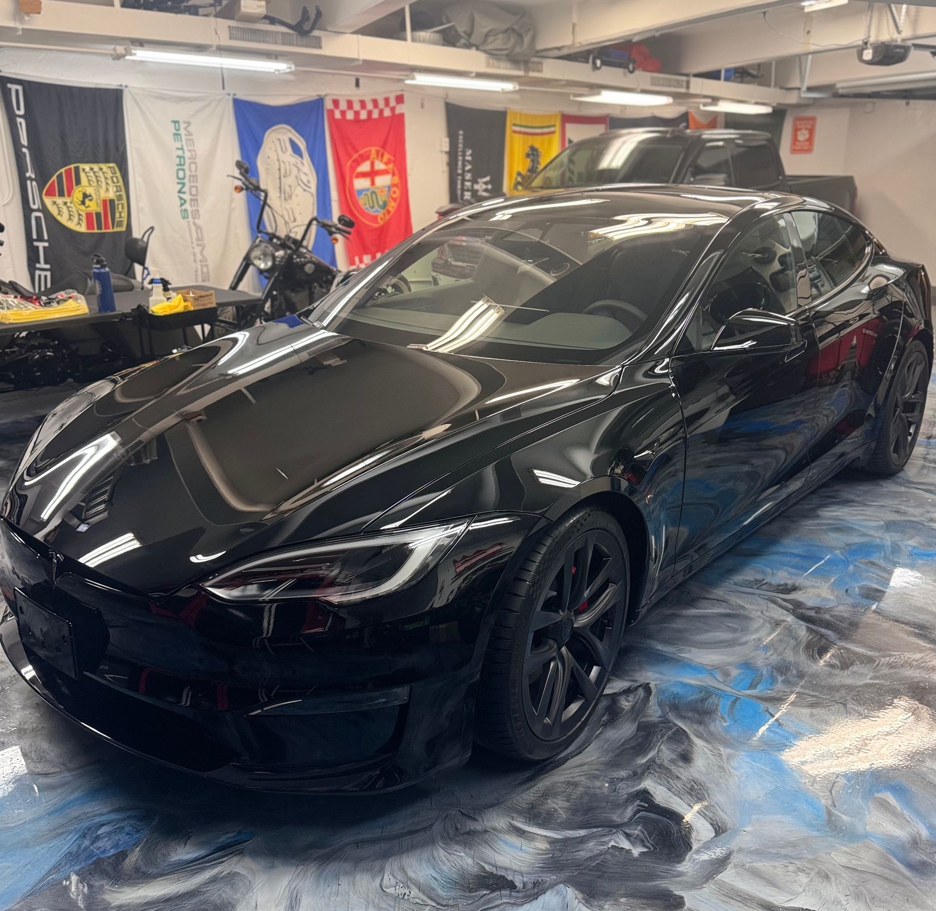 A black sports car is parked in a garage with flags behind it.