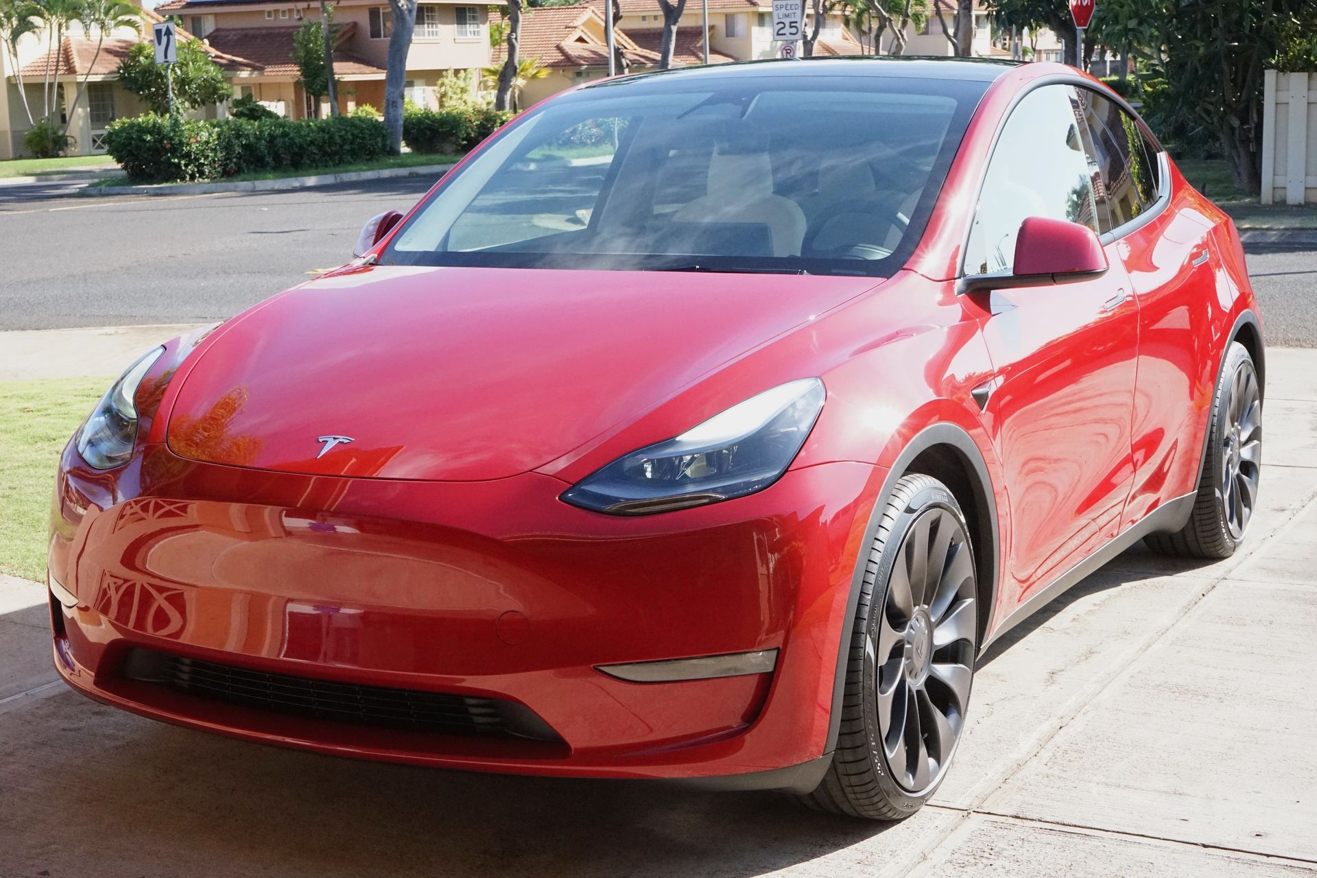 A red tesla model y is parked in a driveway.