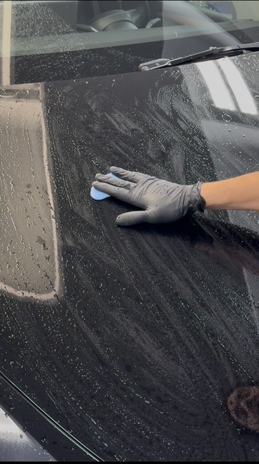 A person is washing a red car with a sponge.