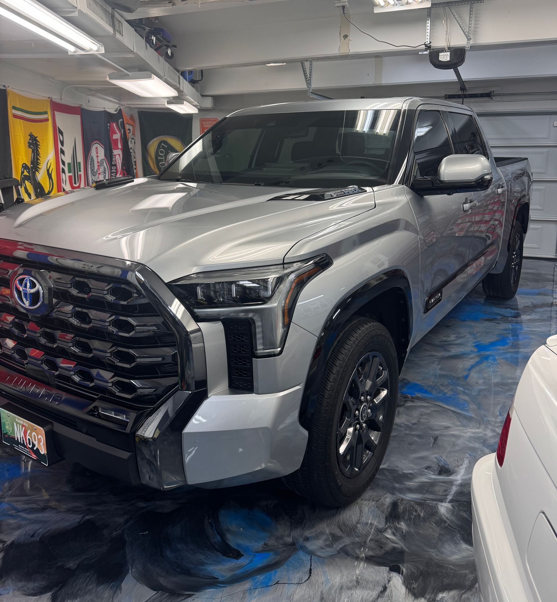 A silver truck is parked in a garage next to a white car.