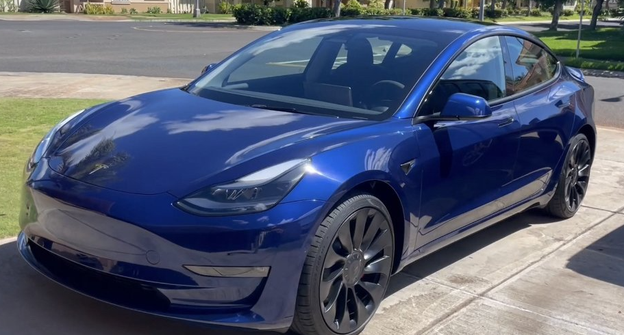 A blue tesla model 3 is parked in a driveway.