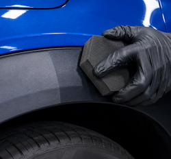 A person wearing black gloves is cleaning a car with a sponge.