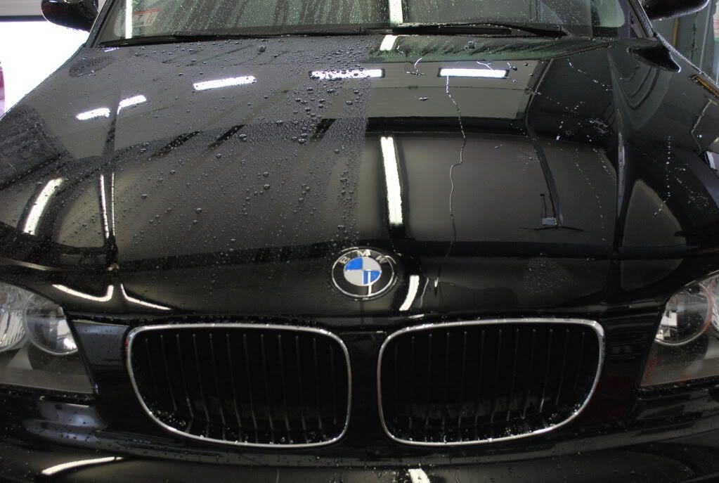 A close up of a black bmw car with water drops on the hood