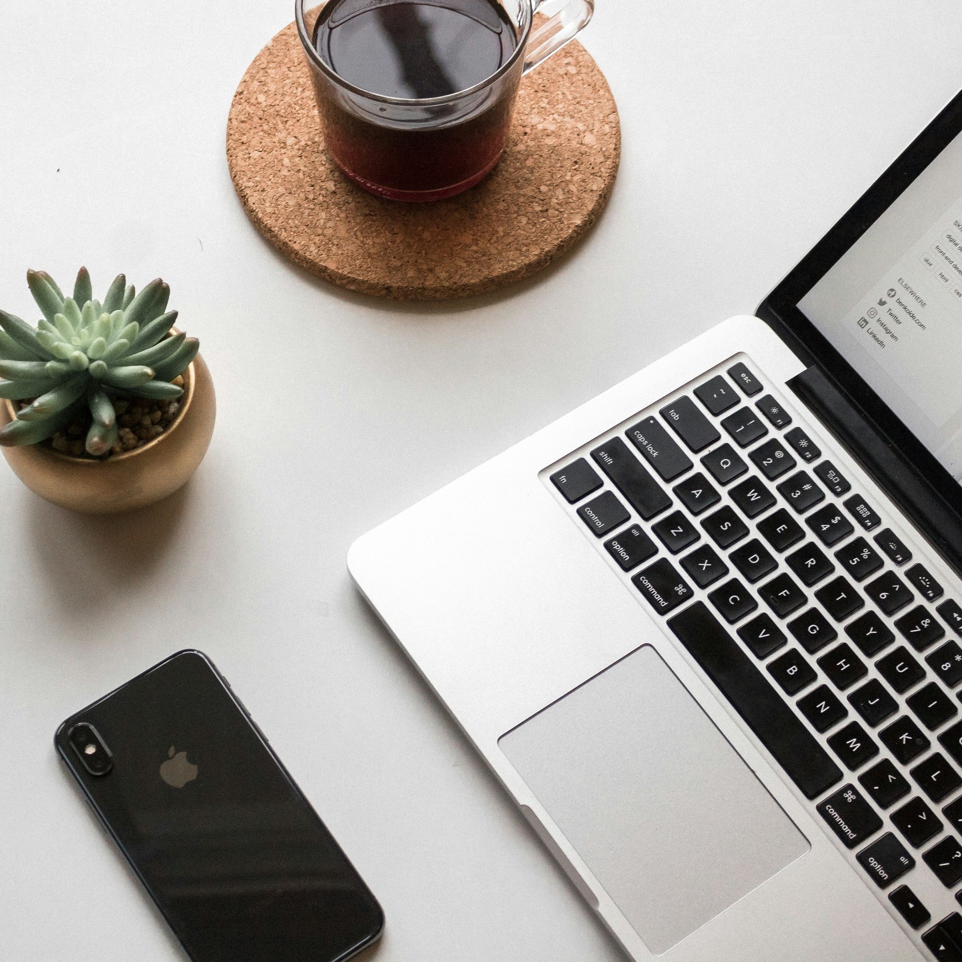 Laptop, coffee, succulent, and phone on a white desk, viewed from above.