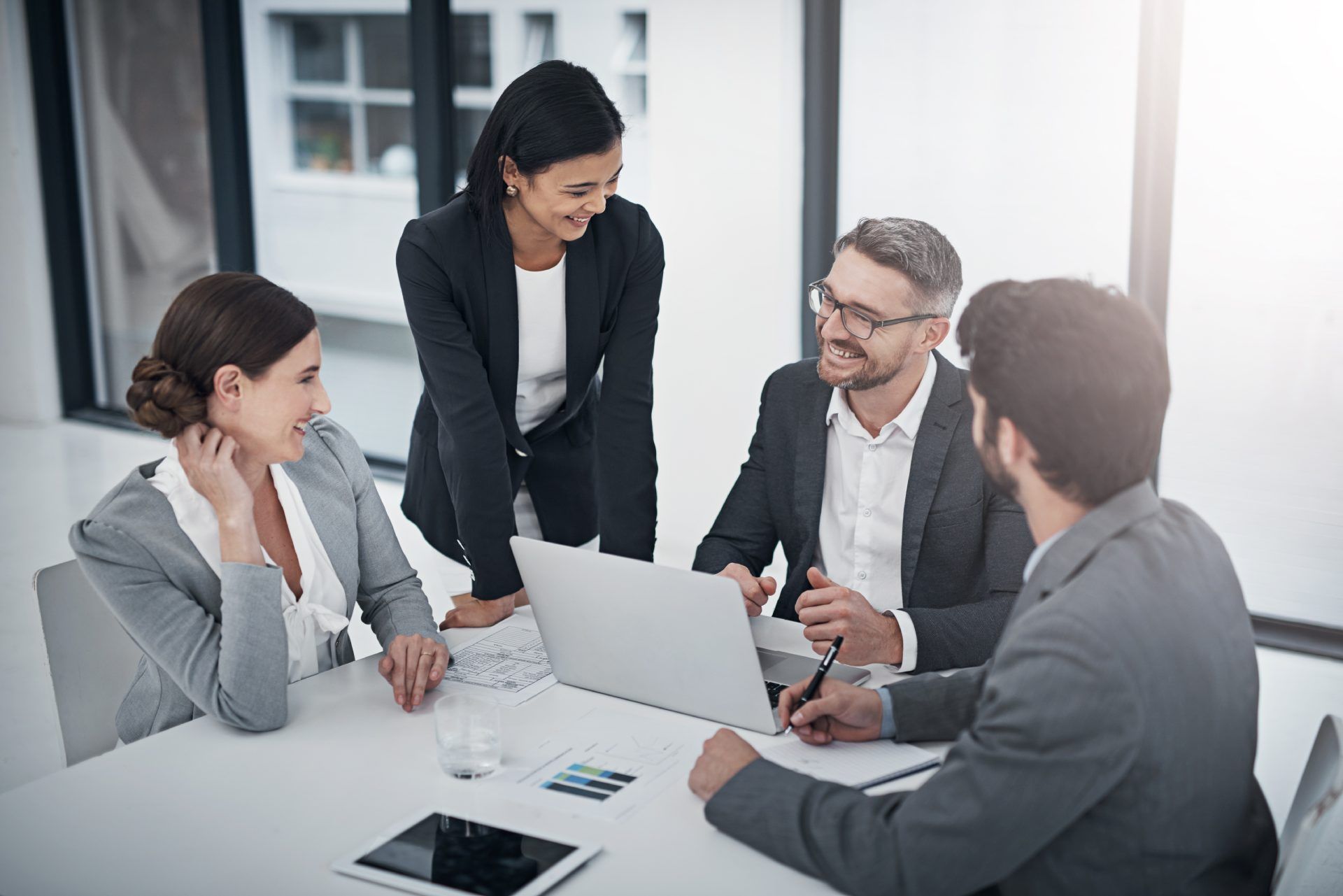 A group of business people are sitting around a table looking at a laptop.