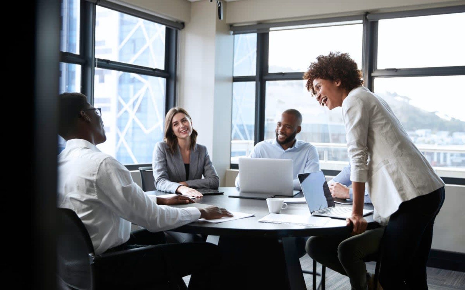 A group of people are sitting around a table with laptops in a conference room.