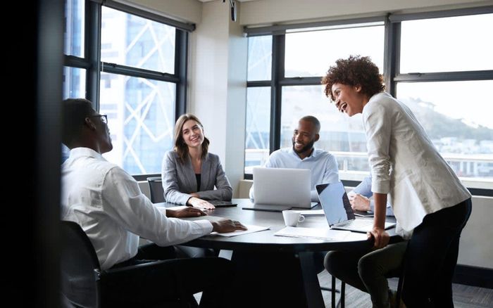 A group of people are sitting around a table with laptops in a conference room.