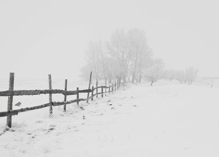 A black and white photo of a wooden fence in the snow.