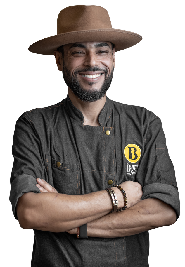 chef iram wearing a hat and a chef 's coat is smiling with his arms crossed .