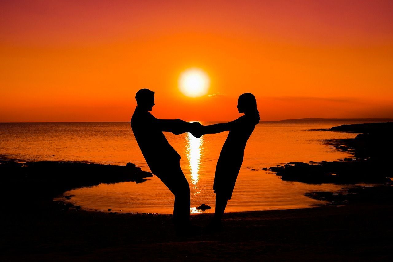 A man and a woman are holding hands on a beach at sunset.