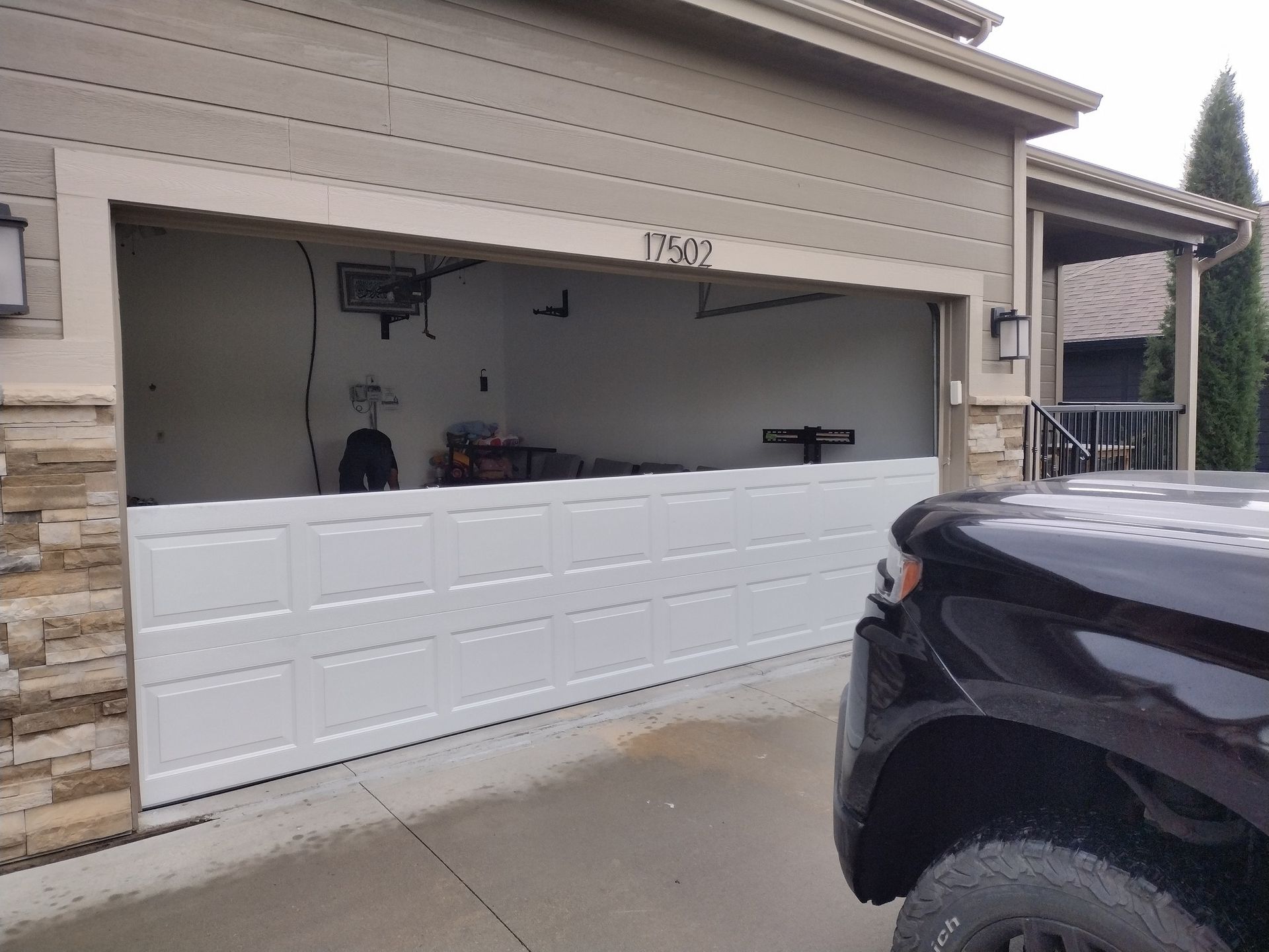 A partially opened white garage door with a view into the interior and a dark pickup truck parked in the foreground.