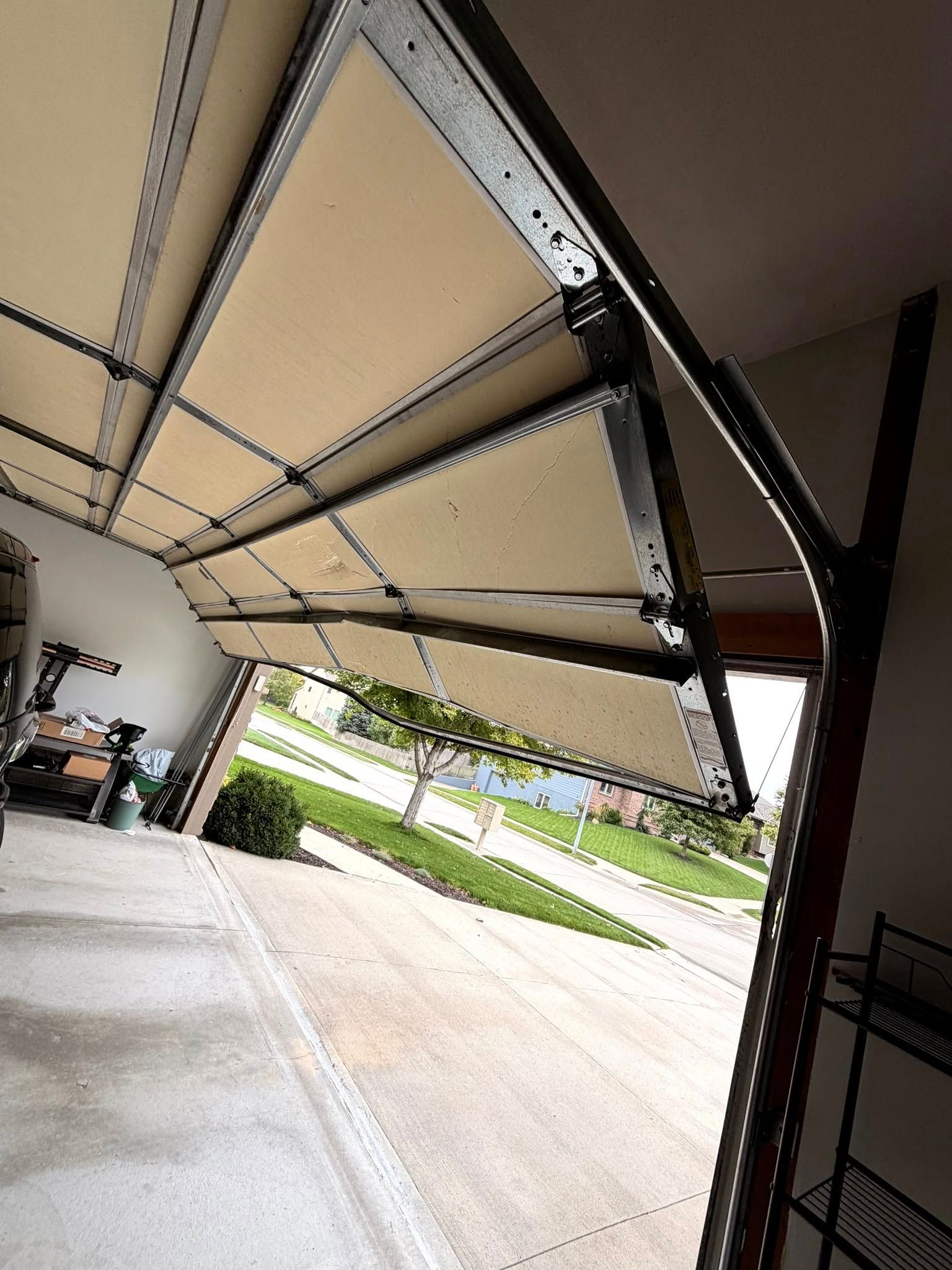 A view from inside a garage looking out through a half-open sectional garage door at a neighborhood street.