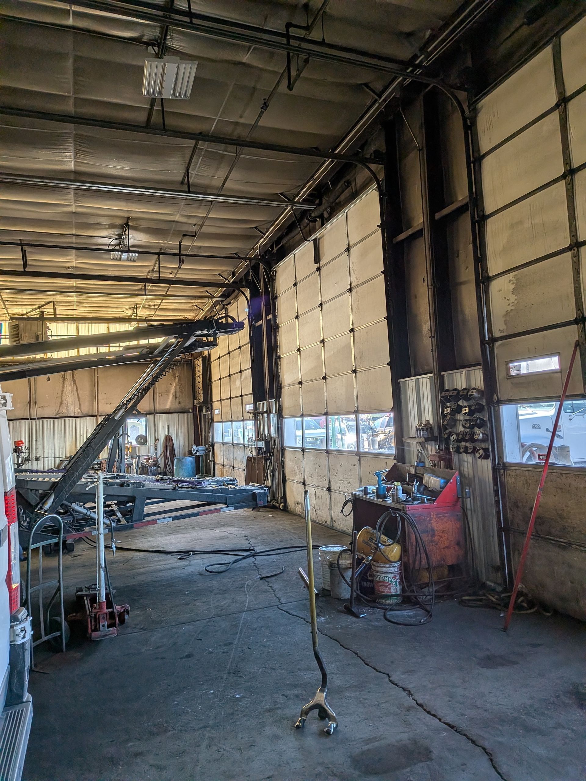A large, dimly lit garage interior with a row of industrial doors showing significant fire and soot damage.