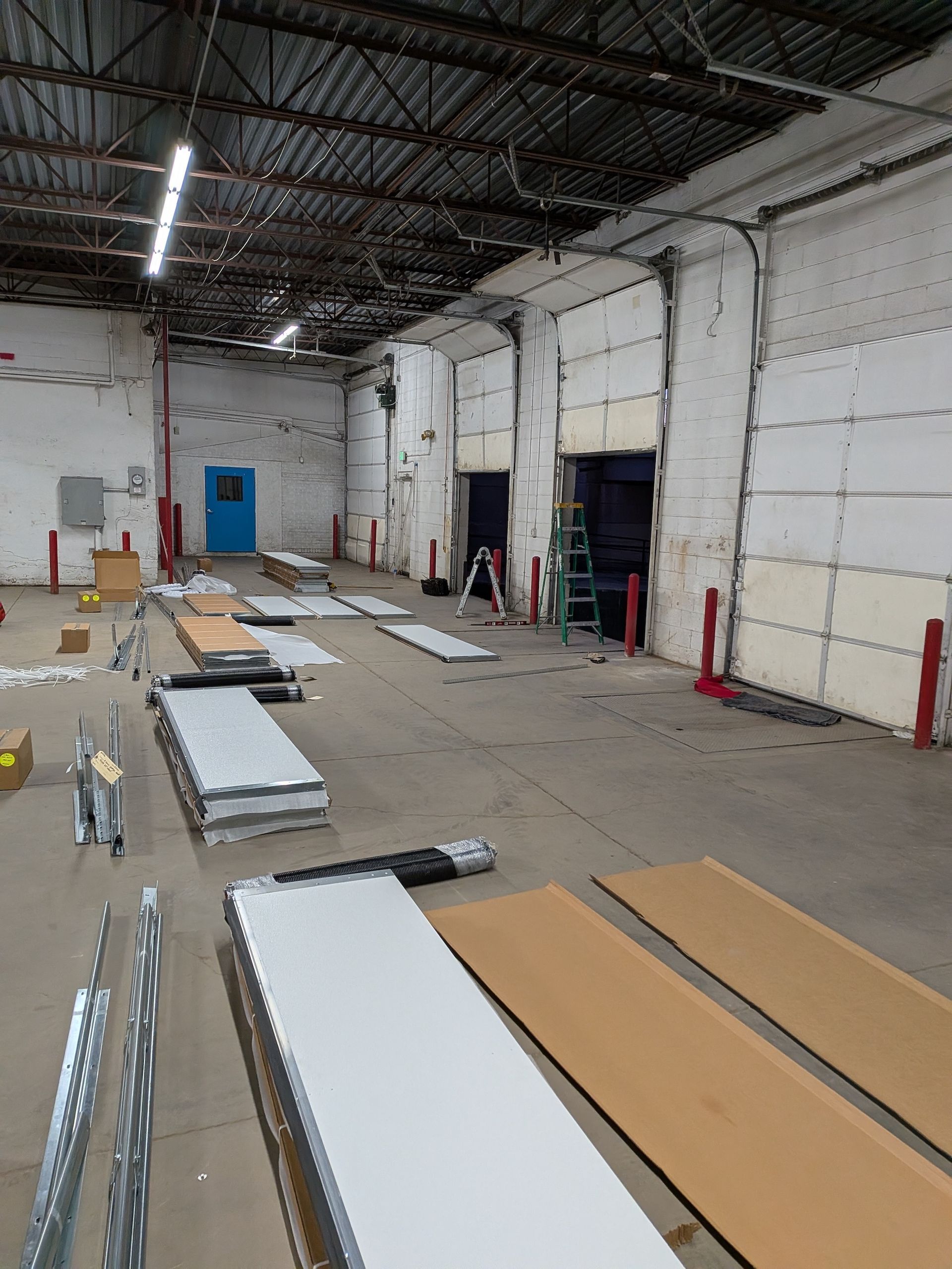 An industrial warehouse interior features concrete floors, loading dock doors, construction materials, and a blue door.