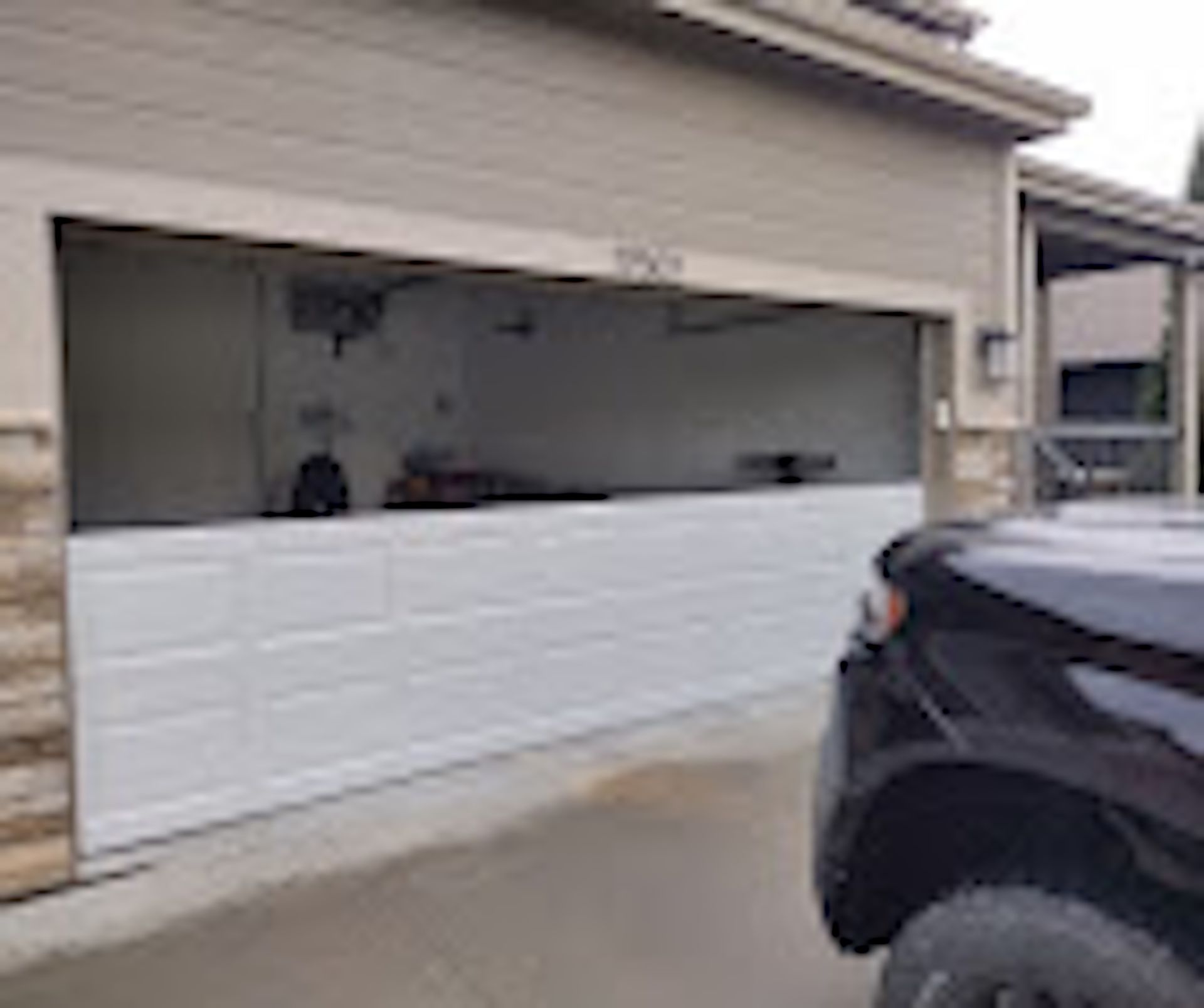 A residential garage with a white door partially raised, revealing a partially empty interior, with a black truck parked.