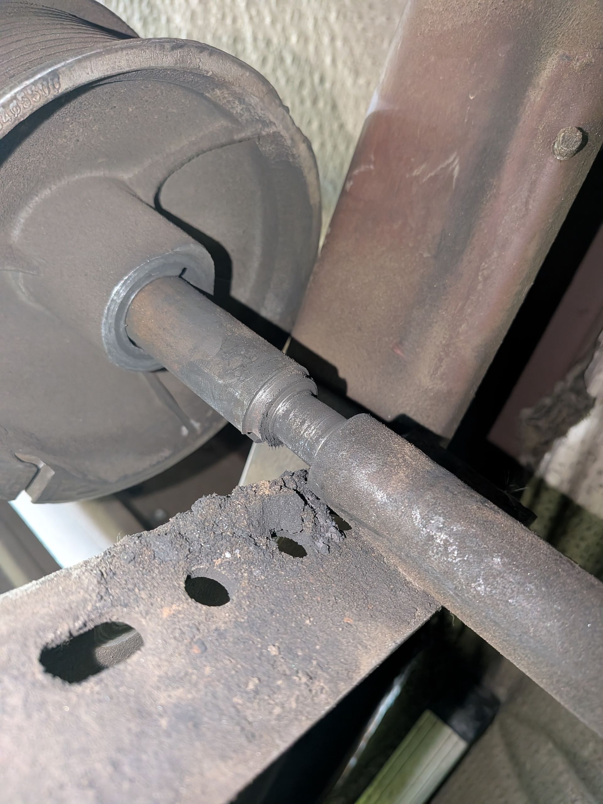 A close-up view shows a rusted metal rod connecting to a wheel mechanism, covered in dark, gritty residue.