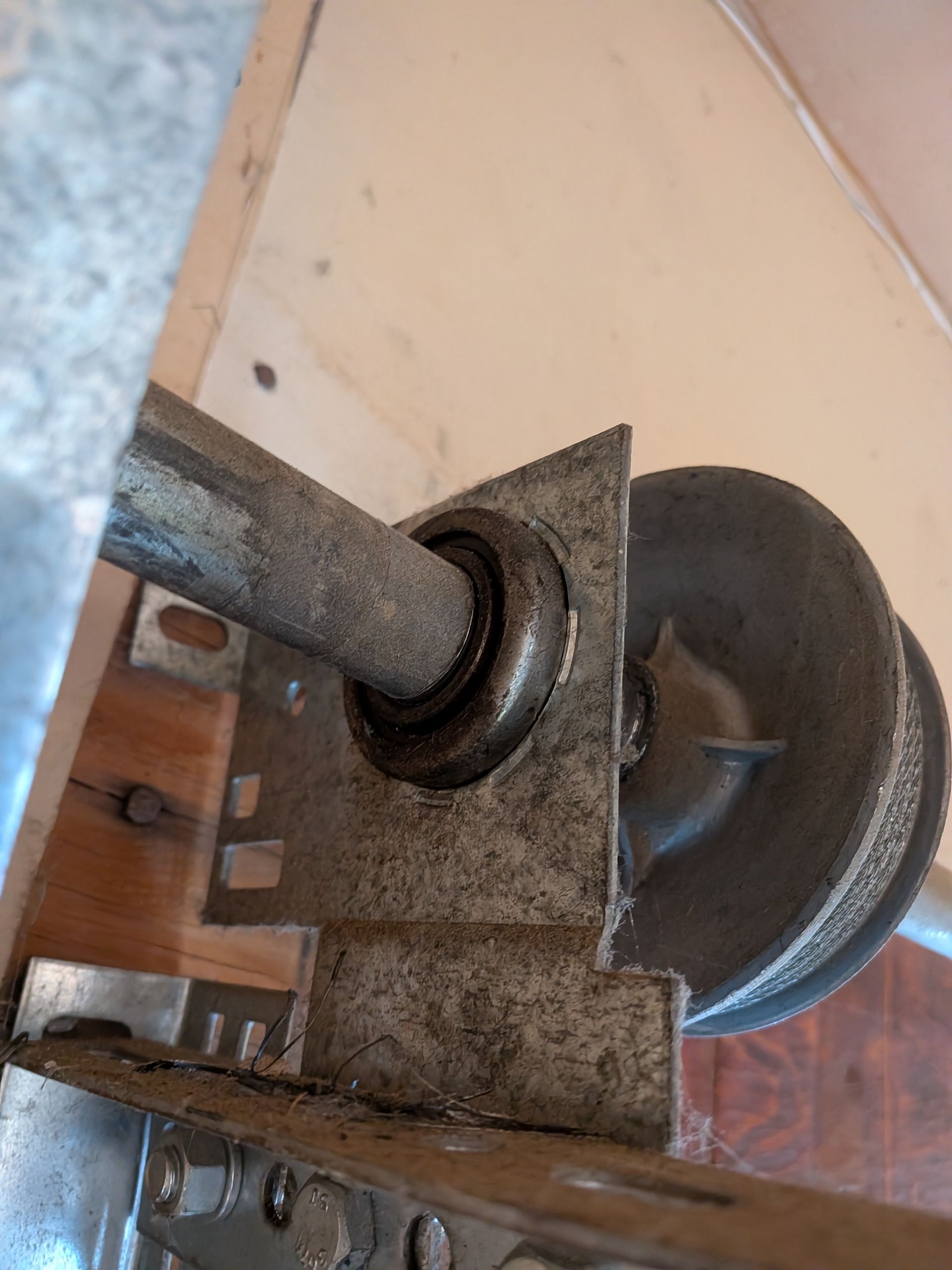 A close-up view of a metal garage door pulley assembly, showing a shaft, a circular bearing, and a mounting bracket.