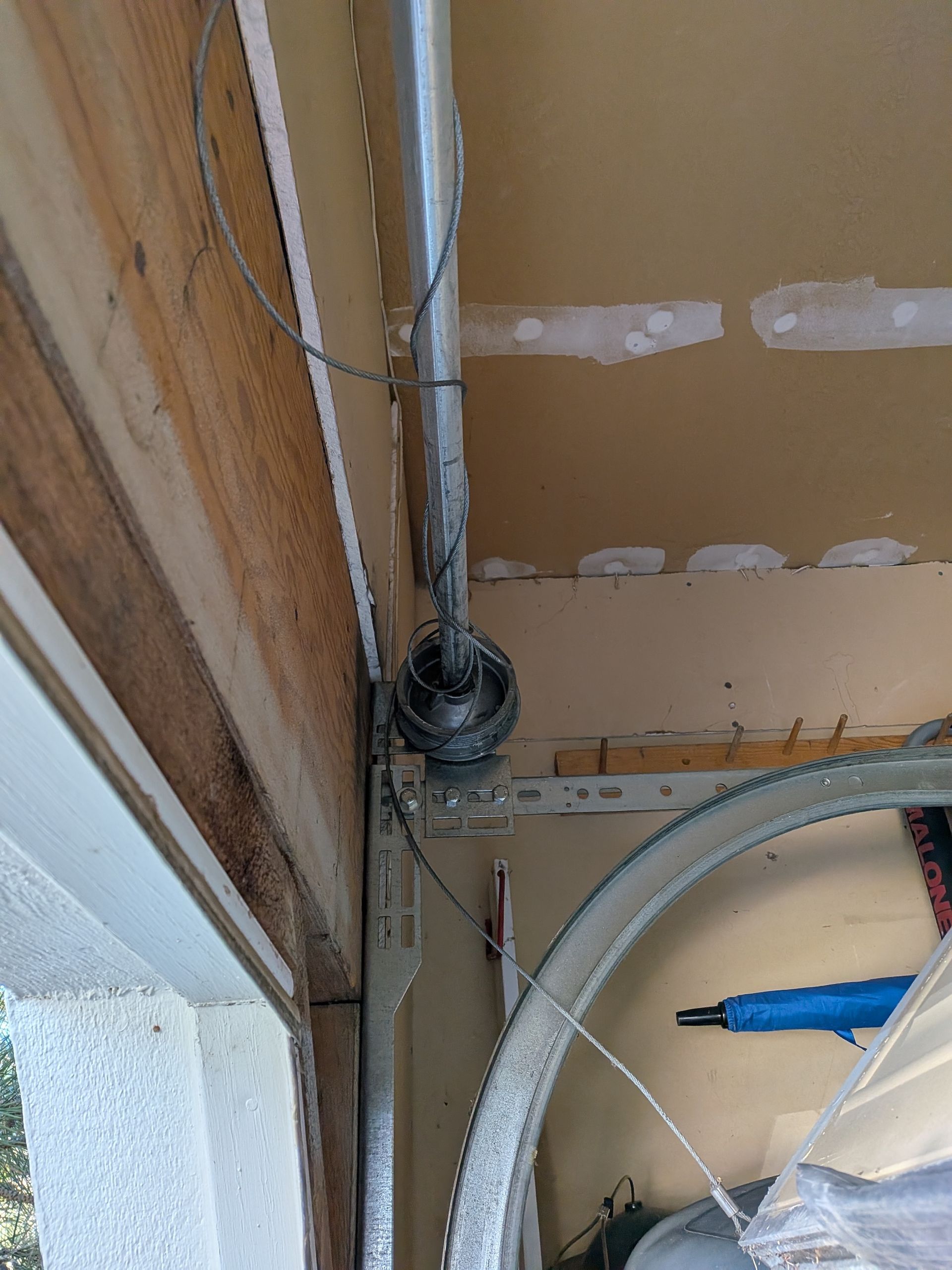 A close-up of a broken garage door cable drum and frayed wire hanging from a metal ceiling track.