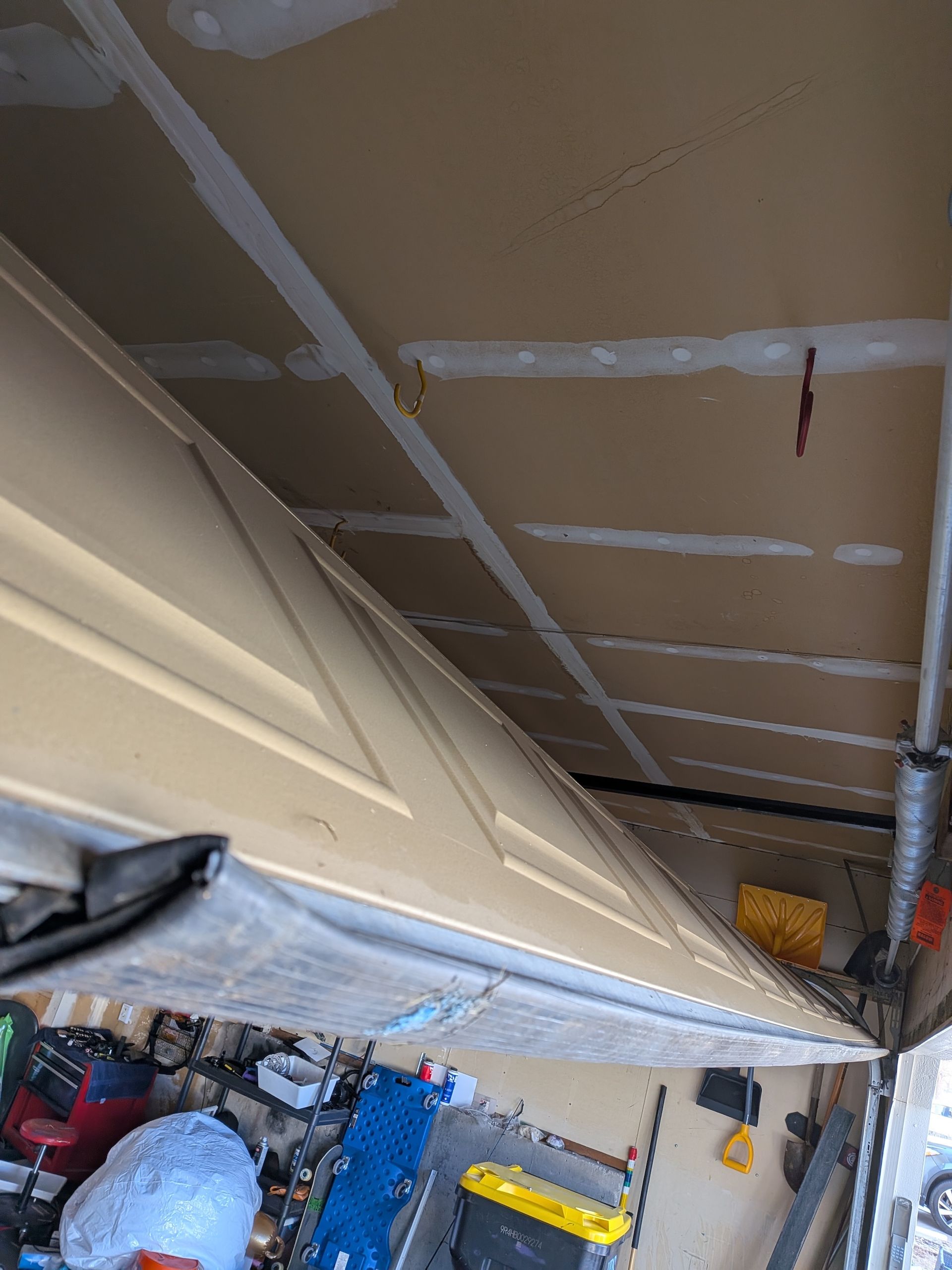 An upward, angled view inside a garage showing a beige door panel and an unfinished drywall ceiling with taped seams.