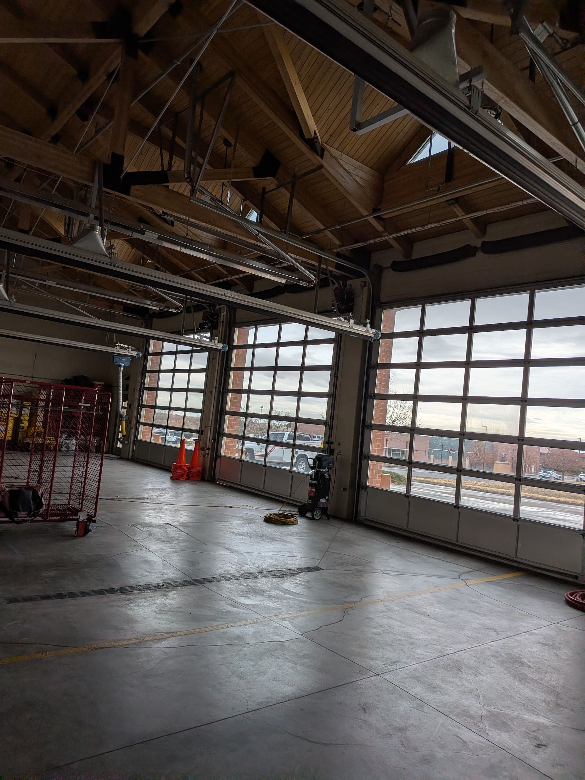 Interior of an empty garage with concrete floors, exposed wood ceiling beams, and large glass paneled doors.