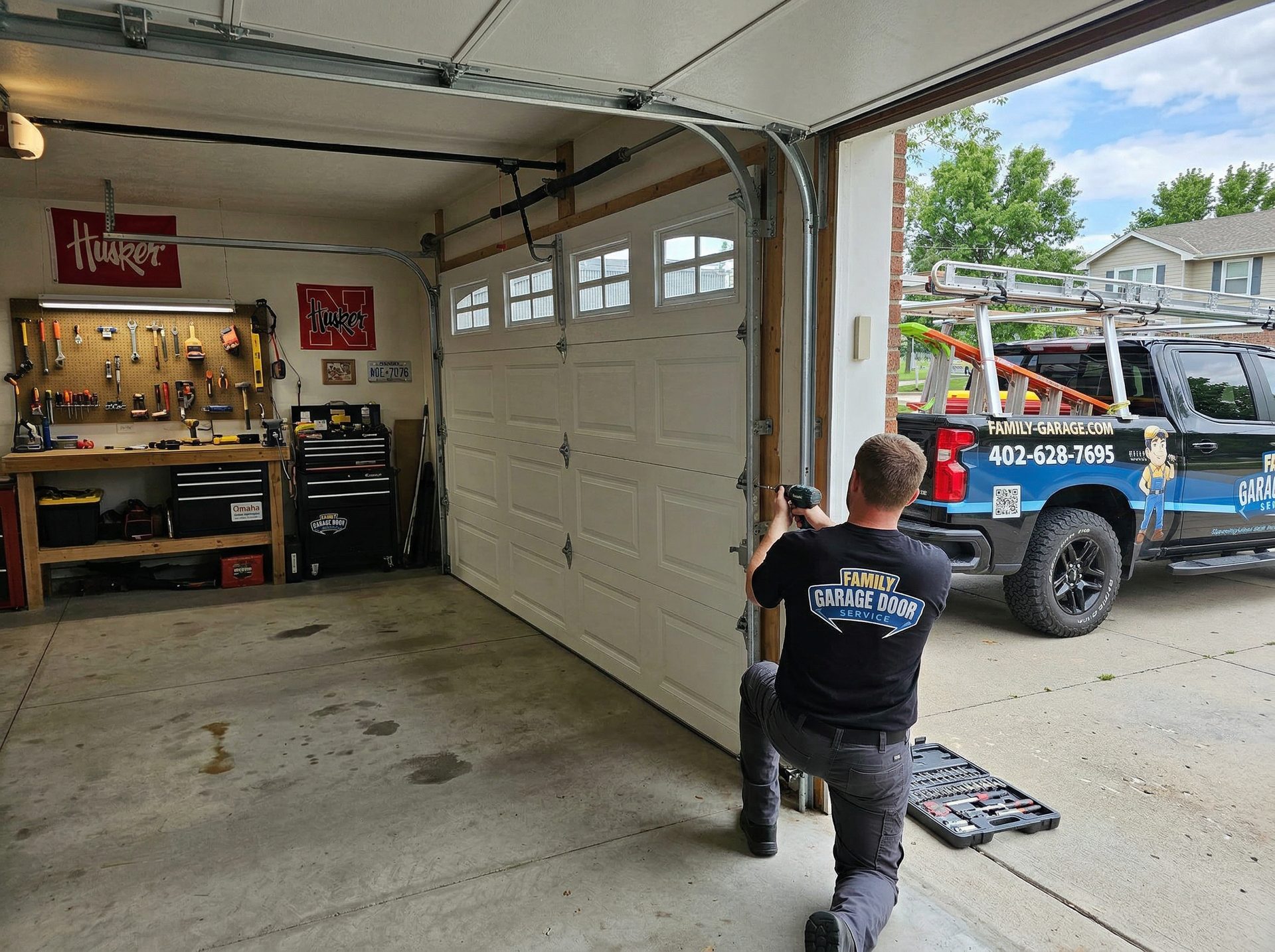 A service technician kneeling to install or repair a residential white garage door in a workshop setting.