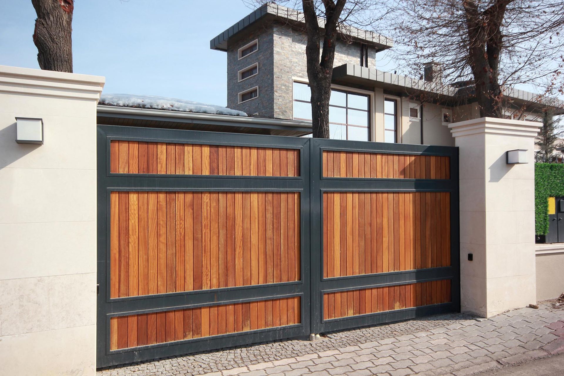 Wooden sliding driveway gate with black metal frame and white pillars