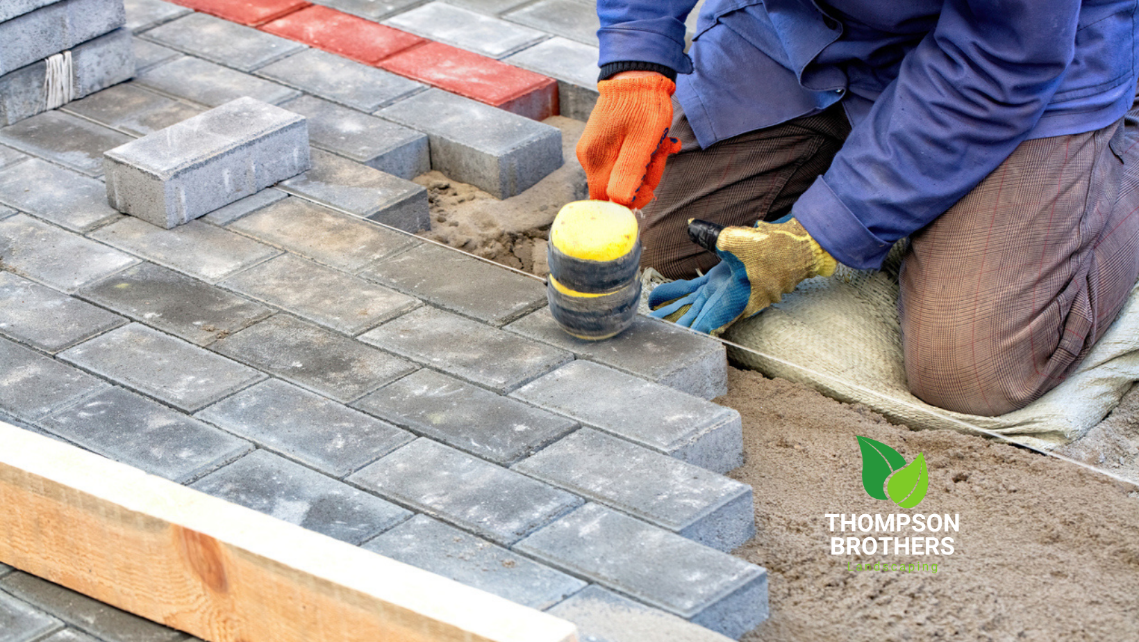 Person laying gray pavers with a rubber mallet. Construction site.