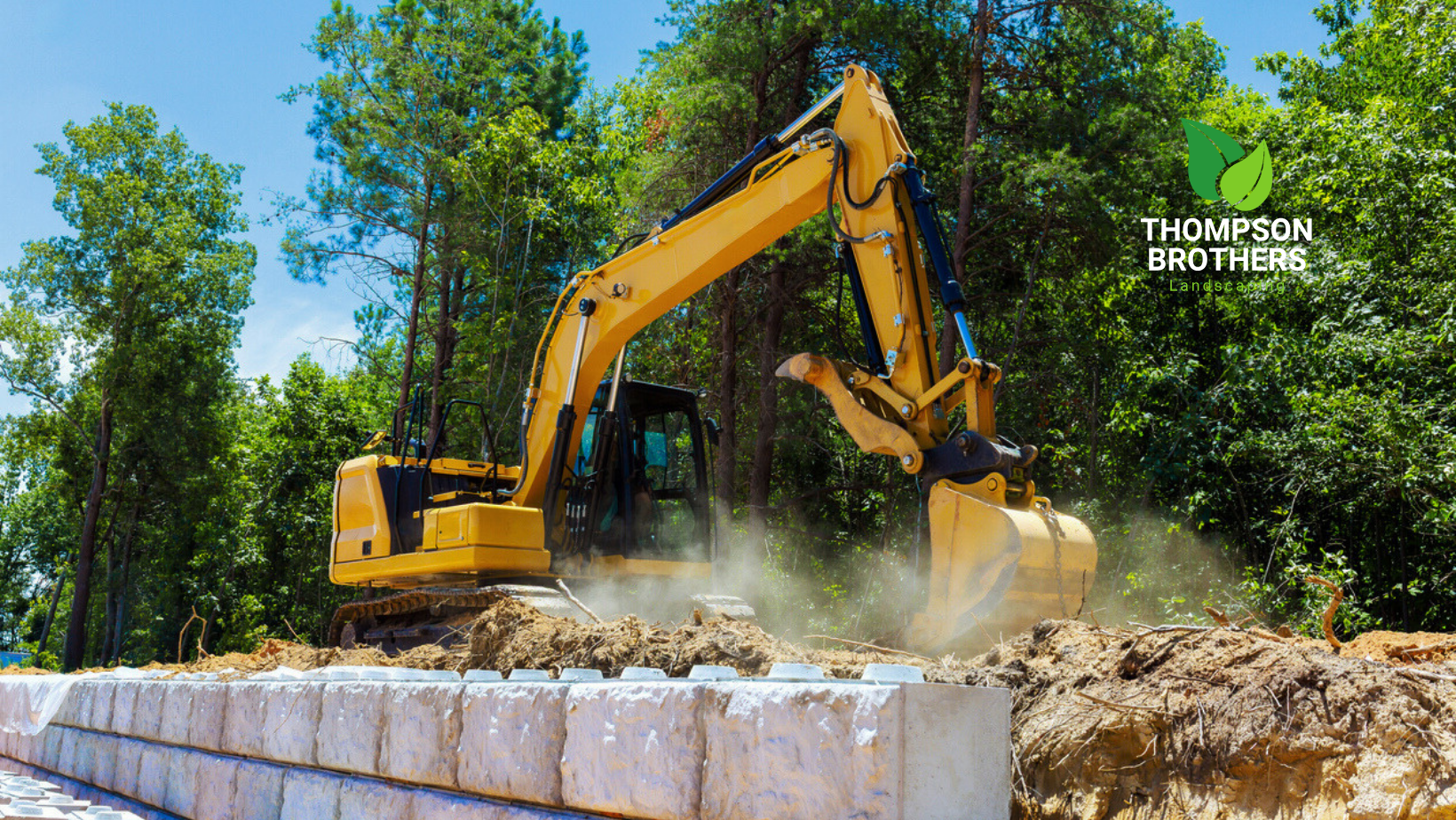 Yellow excavator digging earth next to a block retaining wall, sunny day.