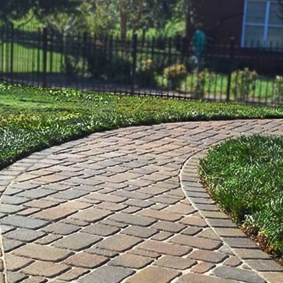 A brick walkway leading to a house with a fence in the background