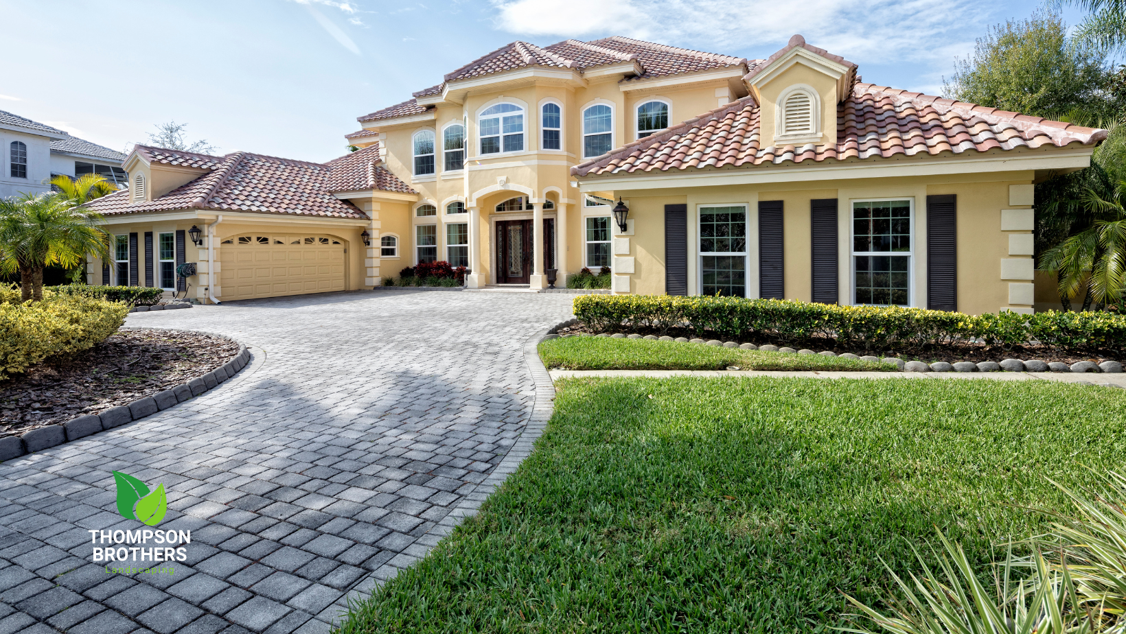 A large yellow house with a hardscapes driveway leading to it.