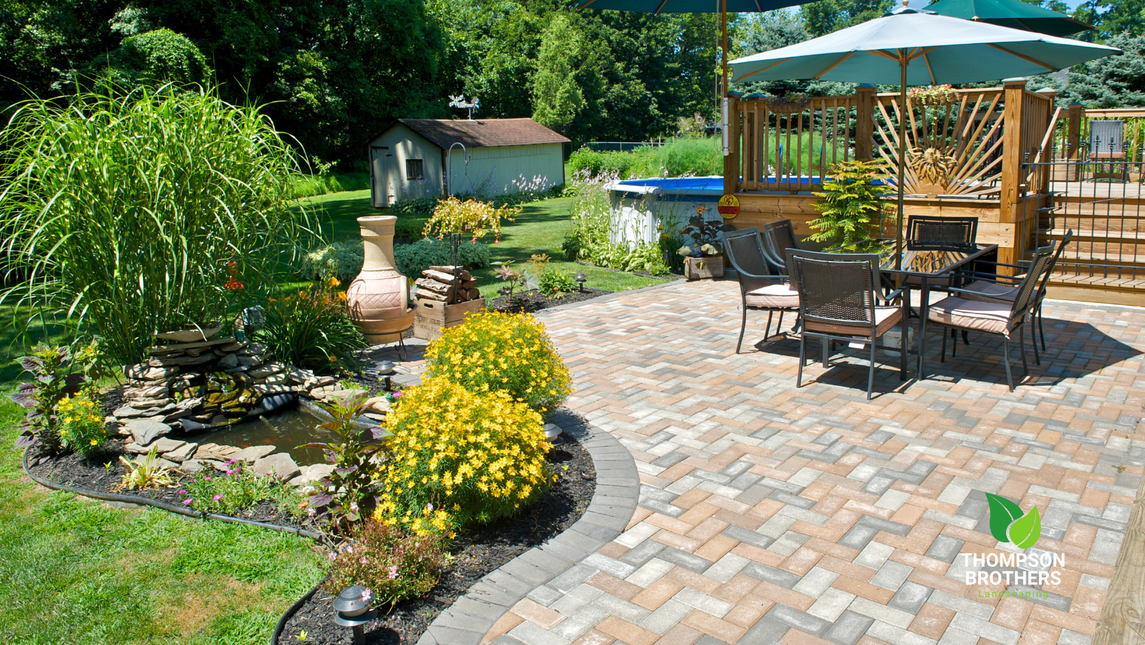 A patio with a table and chairs and an umbrella in a backyard.