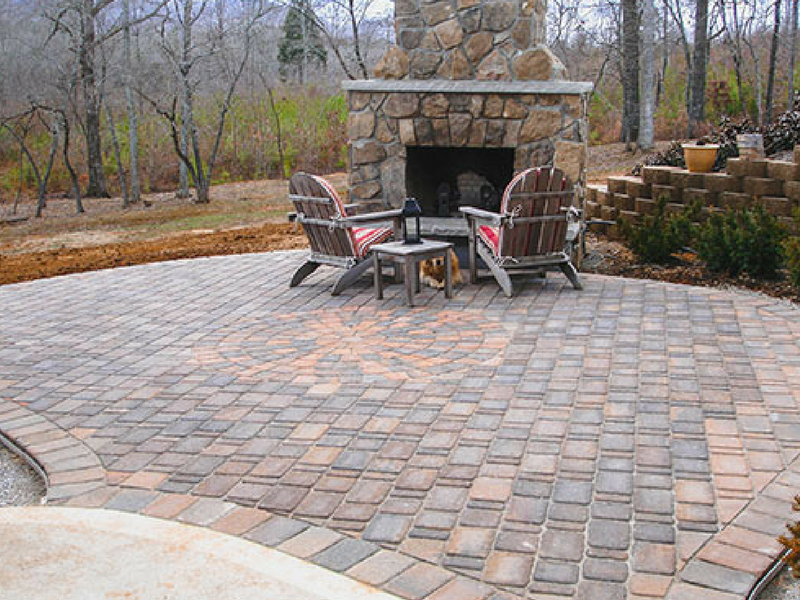 Two chairs are sitting in front of a stone fireplace on a patio.