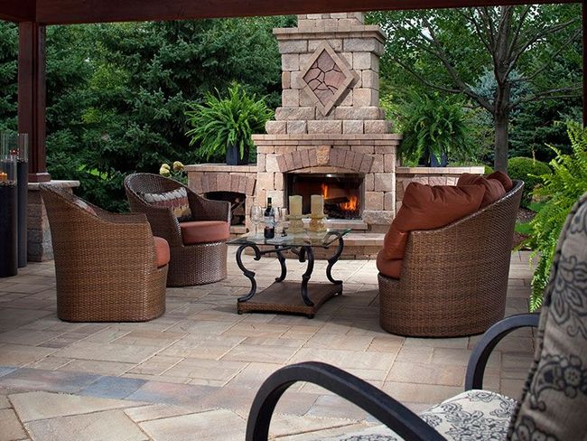 A cozy outdoor patio with a stone fireplace, wicker furniture, and a coffee table under a covered structure.